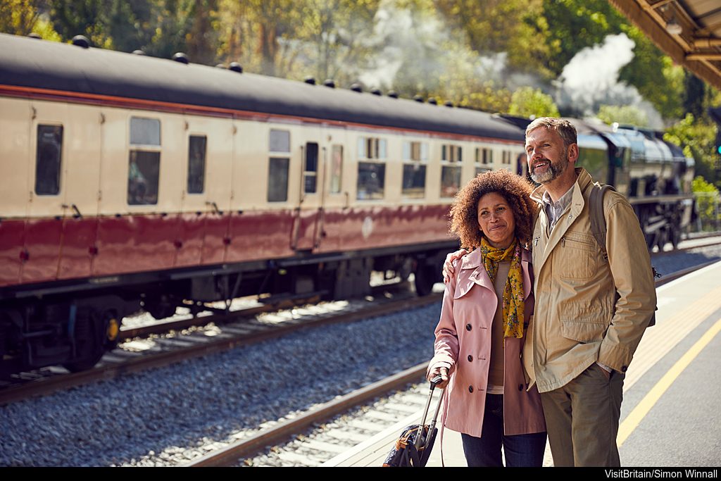 vb34164978   bath station bath england. a steam train the royal scot in steam with carriages on the rails. a couple travellers a man and woman standing on the platform